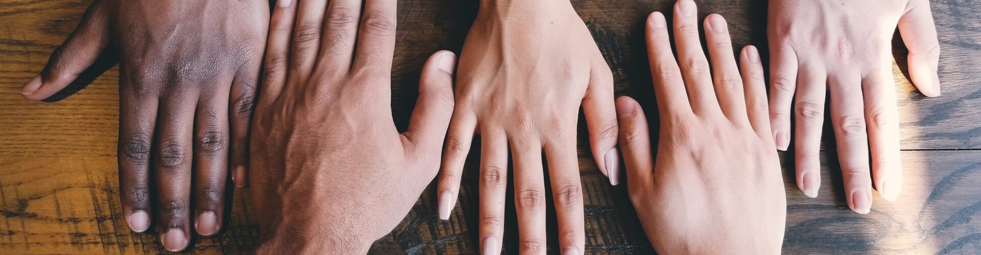 Close up of four people's hands in a row on a wooden table